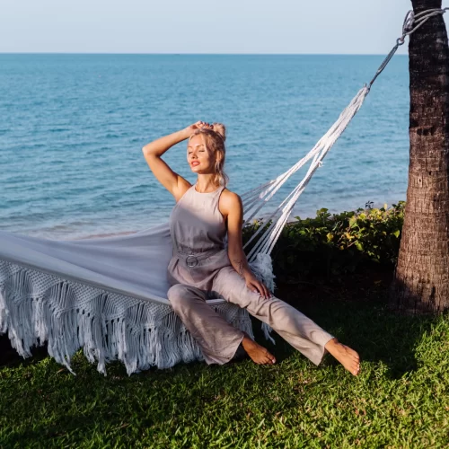 Mujer sentada en una hamaca blanca junto al mar.
