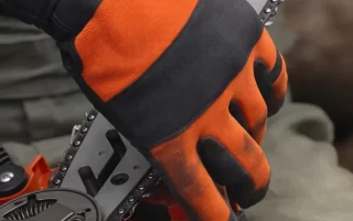 Manos con guantes naranjas y negros colocando la cadena en la espada de una motosierra eléctric