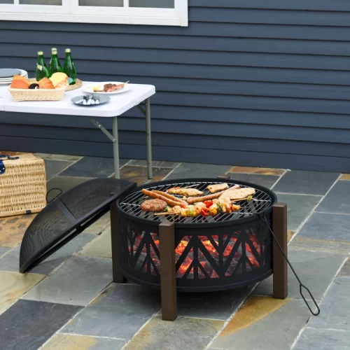 Braseiro em forma de taça com grelha, carne e legumes a assar junto a uma mesa com aperitivos no jardim