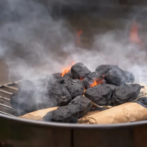 Briquetes de carvão a arder com chamas e fumo no grelhador