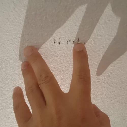 Mão a assinalar os orifícios de teste no teto para localizar a largura da viga.