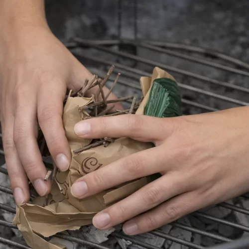 Mãos a colocar pequenos ramos secos sobre papel para acender o carvão