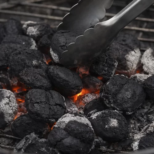 Pinças a movimentar briquetes de carvão quente no grelhador