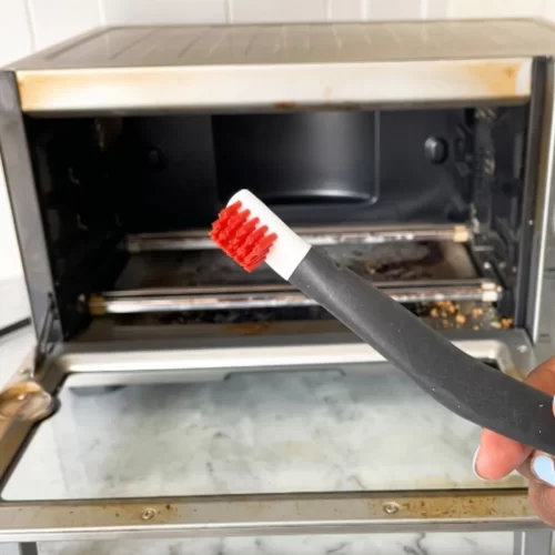 Escova pequena a limpar os cantos de um forno de bancada aberto e sujo.