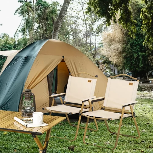 Duas cadeiras de campismo dobráveis de madeira junto a uma tenda de campismo e uma mesa auxiliar