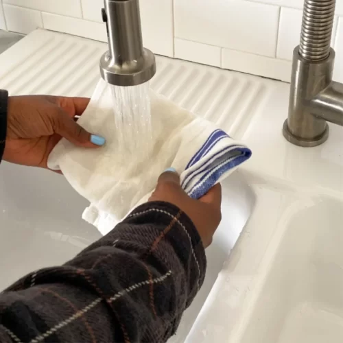 Pano branco a ser enxaguado debaixo da torneira do lava-loiça.