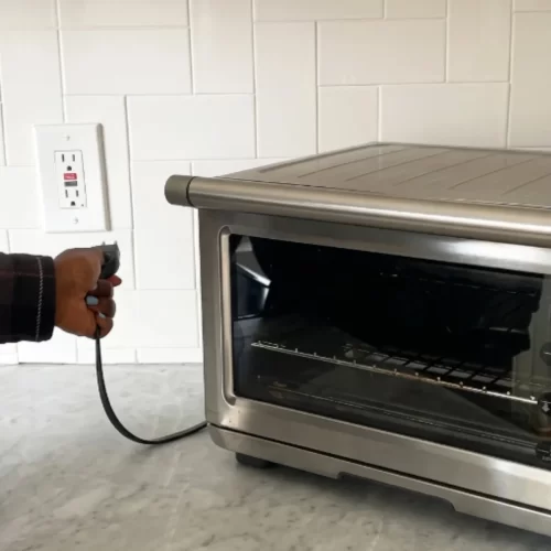 Mão a desligar o forno de bancada da tomada.