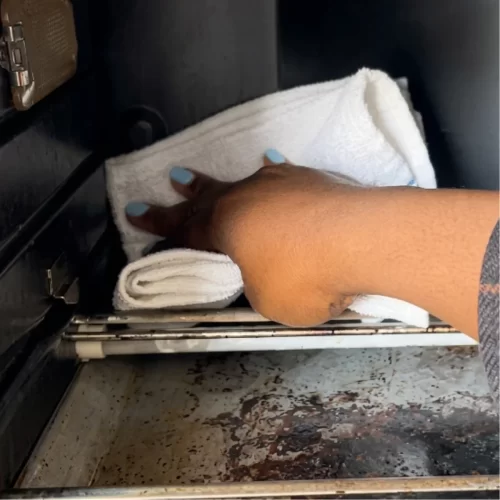 Mão a limpar o interior sujo do forno de bancada com um pano branco.