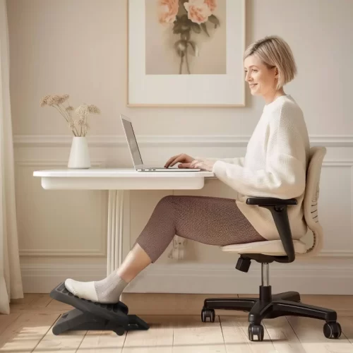 Mulher a trabalhar com um computador portátil e os pés apoiados num apoio para pés