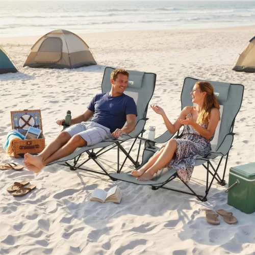 Casal a relaxar em cadeiras de campismo reclináveis com apoio para os pés na praia, junto a tendas de campismo e uma geleira portátil