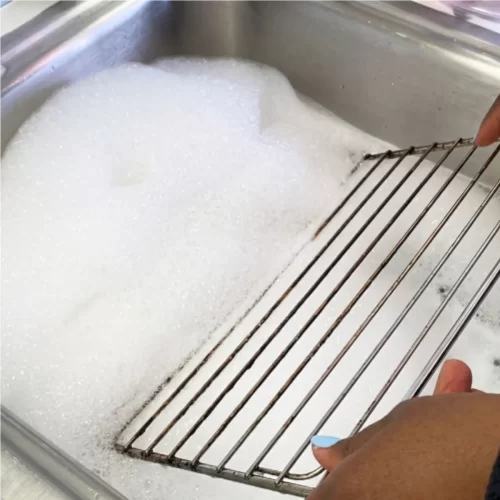Grelha do forno de molho em água com detergente no lava-loiça.