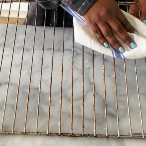 Grelha metálica limpa a ser seca com um pano de cozinha.