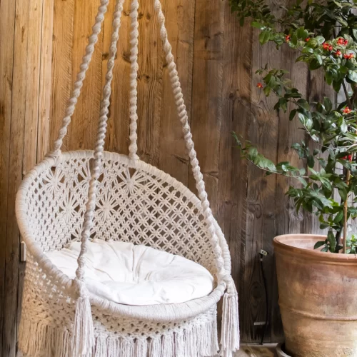 Cadeira suspensa de macramé com franjas e almofada num terraço rústico de madeira